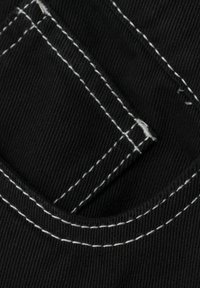 Tela negra con un bolsillo y costura blanca. La textura es acanalada, destacando los detalles de construcción y el contraste en la costura.