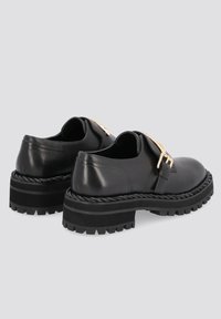 Musta nahkakengät, joissa on paksu pohja ja punottu reuna. Huomattava kultainen korostus ja pyöreä kärkipaino. Näkyvät ompeluyksityiskohdat.