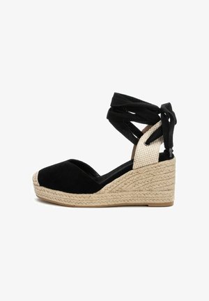 Sandalias de cuña de ante negro con plataforma de yute trenzado, que presentan correas de tela negra entrelazadas y una sección de tobillo texturizada en beige.