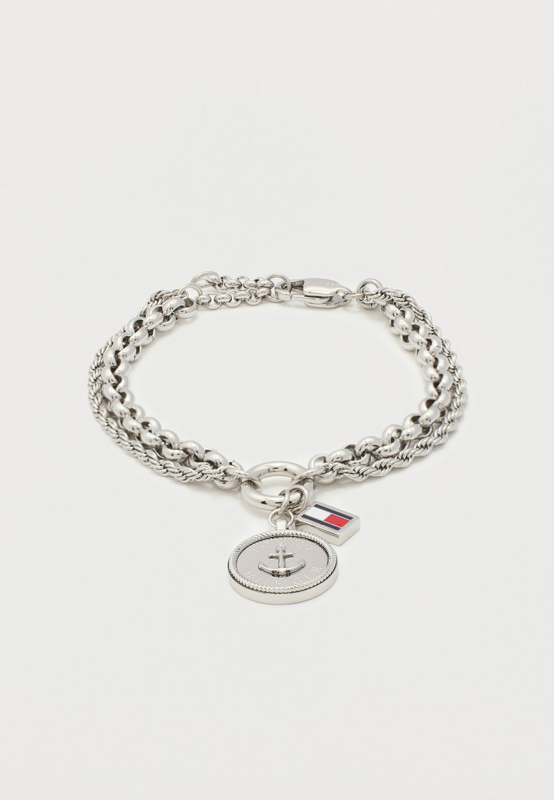 Βραχιόλι αλυσίδας σε ασημί τόνο με δύο γούρια: ένα στρογγυλό μενταγιόν άγκυρας με χαραγμένο το "Tommy Hilfiger" και μία ορθογώνια σημαία με κόκκινο, λευκό και μπλε.