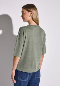 Zielona, teksturowana koszulka z krótkim rękawem i okrągłym dekoltem, zestawiona z niebieskimi dżinsami. Materiał wydaje się miękki i swobodny.