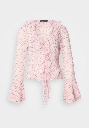 Růžová halenka s volánkovým výstřihem a zvonovými rukávy, zdobená vzorem puntíků v tmavší růžové barvě a zavazovací detaily na přední části.
