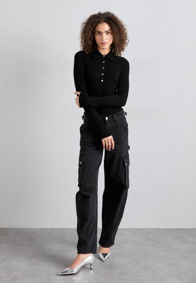 Polo shirt noir à manches longues avec un plastron boutonné, associé à un pantalon cargo noir avec poches latérales, et des chaussures à talons hauts argentées.