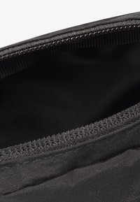 Svart tygpåse med dragkedjestängning, med en slät yta och förstärkta kanter. Insidan är också svart och behåller en minimalistisk design.