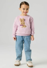 Helelilla dressipluus, millel on tekstuuriga jänkuapplikaatsioon pruunide karvade ja lillaka vööga, kombineeritud siniste teksade ja valgete kingadega.