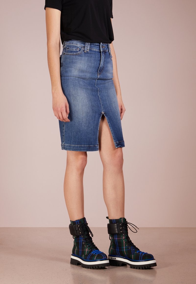 Žena oblečená v modré džínové sukni ke kolenům s předním rozparkem a černých, modrých a zelených kostičkovaných šněrovacích botách s tlustou podrážkou.