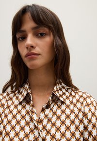 Bruin en wit gestreept shirt met een kraag, voorzien van geometrische ontwerpen en knoopaccenten, gemaakt van lichtgewicht stof.