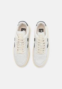 Sneakers bianchi in pelle con design forato, lacci beige e dettagli blu navy. Presentano una suola in gomma e un evidente logo "V" sul lato.