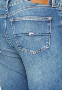Denim jeans in medium blue, featuring a textured finish, five-pocket design, and a small red, white, and blue logo on the back pocket.