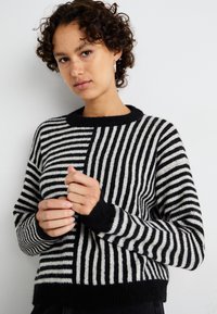 Maglione a righe in bianco e nero realizzato in maglia, caratterizzato da diverse trame a righe, scollo rotondo e polsini a coste. Tessuto caldo e testurizzato.