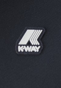 Logo K-WAY su uno sfondo in tessuto blu navy scuro. Il logo presenta una lettera 'K' stilizzata con tre linee diagonali bianche.