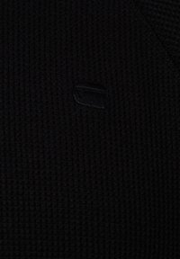 Schwarzer strukturierter Stoff mit einem gerippten Design, in das ein kleines, geprägtes Logodetail eingearbeitet ist.