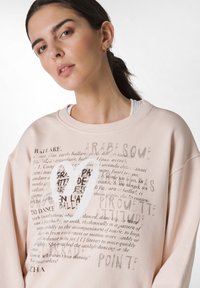 Jasnoróżowy sweter z grafiką tekstu i wzorem serca. Okrągły dekolt, luźny krój, miękka tekstura i casualowy styl.