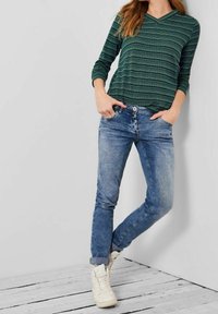 Grön- och blårandig långärmad topp som matchas med ljusblå jeans och vita sneakers. Outfiten har en avslappnad passform med uppvikta ärmslut.