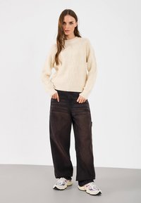 Maglione crema a maglia grossa con maniche lunghe abbinato a pantaloni larghi neri e sneakers multicolori. Tessuto liscio, vestibilità comoda.