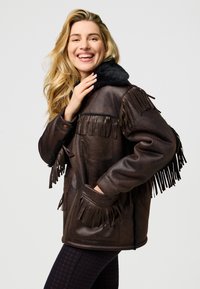 Ruda odinė striukė su kutais, juodu sintetiniu kailio apykakle, užtrauktuku ir dviem priekinėmis kišenėmis. Lygi tekstūra. Stilingas dizainas.