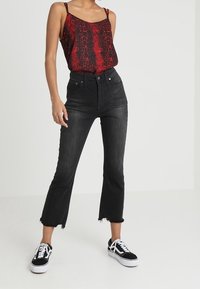 Jean noir taille haute avec ourlet brut, associé à un débardeur rouge à motifs. Des baskets noires avec des accents blancs complètent la tenue.