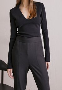 Svart långärmad topp med V-ringning, kombinerad med högmidjade svarta byxor med stilrena sömnadsdetaljer. Slät, figurnära tyg.