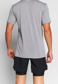 Grå kortärmad träningströja med en jämn yta, i kombination med svarta shorts med ett lagerdesign och ventilerande tyg.