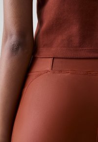 Rūsganas pieguļošs tops un legingi, kuriem ir gluda, elastīga tekstūra un kārtīgas šuves gar šuvēm. Nav redzamu rakstojumu vai detaļu.