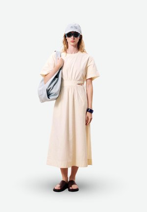 Femme portant une robe midi beige, une casquette blanche, des lunettes de soleil bleues, un bracelet noir, des sandales marron et portant un grand sac cabas gris clair sur l'épaule.