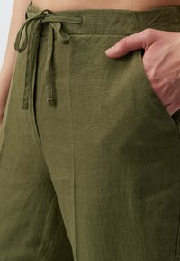 Olivgrüne Leinenhose mit Bindegürtel, seitlichen Taschen und strukturiertem Stoff in lockerer Passform.