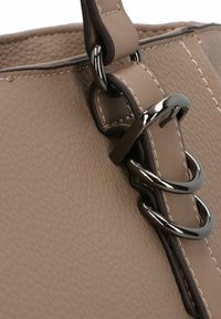 Beige strukturiertes Handtaschenmaterial mit dunkelbraunen Akzenten, ausgestattet mit einem dicken Tragegurt, der durch glänzende Metallringe und kontrastierende Nähte gesichert ist.