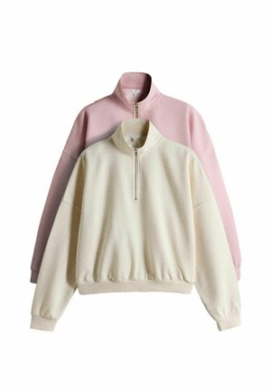 Two quarter-zip fleece sweatshirts, one cream in front and one light pink behind, both with long sleeves and stand collars.