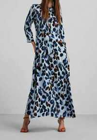 Abito lungo di colore azzurro chiaro, con stampa leopardo nera e marrone. Maniche lunghe, design con bottoncini sul davanti, dotato di tasche e vestibilità fluida.