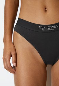 Zwarte katoenen bikini slipjes met een zachte tailleband, voorzien van witte geborduurde tekst "Marc O'Polo EST. IN STOCKHOLM." Glad materiaal, nauwsluitend ontwerp.