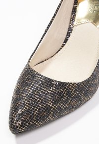 Pompe à bout pointu noire et dorée avec une surface texturée et pailletée, et un revêtement intérieur lisse ; présente des accents métalliques subtils.