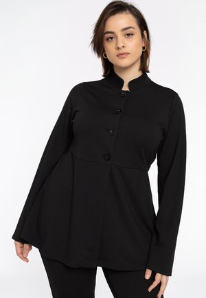 Haut noir à manches longues avec un col mandarin, présentant un buste ajusté, un ourlet évasé et six boutons sur le devant. Texture de tissu lisse.