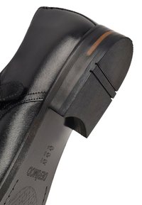 Zapato de cuero negro con punta redondeada. Textura suave, pequeño acento en el lateral, suela de goma con agarre texturizado y ligera elevación del tacón.