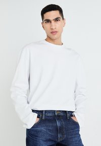 White long-sleeve shirt with a round neck, paired with dark blue denim jeans. Features relaxed fit and simple design without patterns.