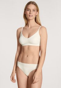 Lichte crème draadloze bh met brede banden en een v-hals ontwerp, vergezeld van bijpassende naadloze bikini slipjes, beide in soepele, rekbare stof.