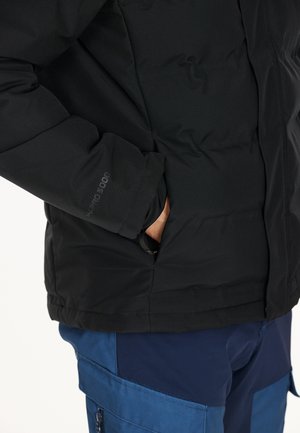 Sort pufferjakke med en glat tekstur, med en sidelomme og "WP5000" branding på ærmet. Kombineret med blå bukser.