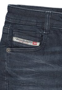 Jeans in denim scuro con una finitura texturizzata, dotati di un'etichetta bianca nella tasca posteriore che riporta la scritta "Diesel Industry Denim Division."