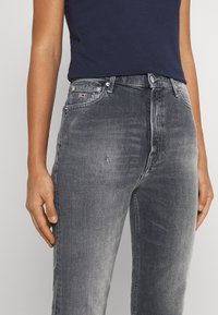 Denim jeans in dark gray with a slightly distressed texture, five-pocket design, and a small embroidered logo on the waistband.