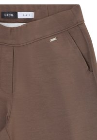 Pantalon marron avec des détails de couture sur le devant, une poche latérale inclinée et une petite étiquette de marque argentée près de la ceinture portant la mention "CECIL".