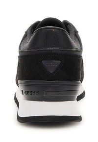 Baskets noires combinant cuir texturé et daim. Semelle intermédiaire blanche remarquable avec le logo "GUESS" à l'arrière.