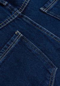 Ciemnoniebieska tkanina denimowa z teksturową powierzchnią, widocznymi szwami i detalem kieszeni w lewnym dolnym rogu.