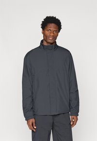 Veste légère gris foncé avec un col haut, des manches longues, des poignets élastiques et un design minimaliste. Texture lisse, sans motifs visibles.