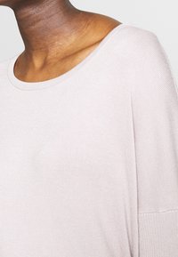 Light pink, ribbed knit top with a wide, rounded neckline and relaxed fit, featuring dropped shoulders and a smooth texture.