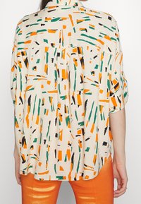 Multi-colored shirt featuring an abstract pattern in orange, green, and black on a cream background. Lightweight fabric with a loose fit.