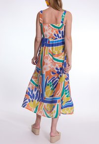 Meerkleuren, enkellange jurk met een gesmokte taille en brede banden, met gedurfde geometrische en bloemige patronen in oranje, blauw, groen en geel.
