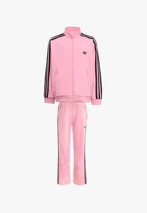 Różowy dres Adidas z czarnymi paskami po bokach, kurtka na zamek z wysokim kołnierzem oraz dopasowane spodnie z elastycznym pasem i kieszeniami.