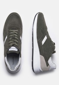 Sneakers in suede verde oliva con accenti bianchi e grigi chiari, dotati di una tomaia perforata, lacci tondi e suola in gomma nera.