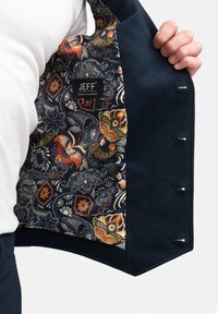 Blazer navy con un exterior texturizado. El interior presenta un patrón de paisley floral en naranja, amarillo, azul y blanco; incluye una etiqueta de la marca.