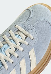 Blauwe suede sneakers met off-white accentstrepen, gestructureerde veters en een gum rubberen zool. Close-up van het materiaal en de stikdetails.