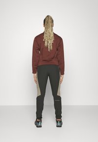 Brun sweatshirt, mörkgröna byxor med beige accenter, och grå träningsskor. Texturerad tyg med en figurnära design, sedd bakifrån.